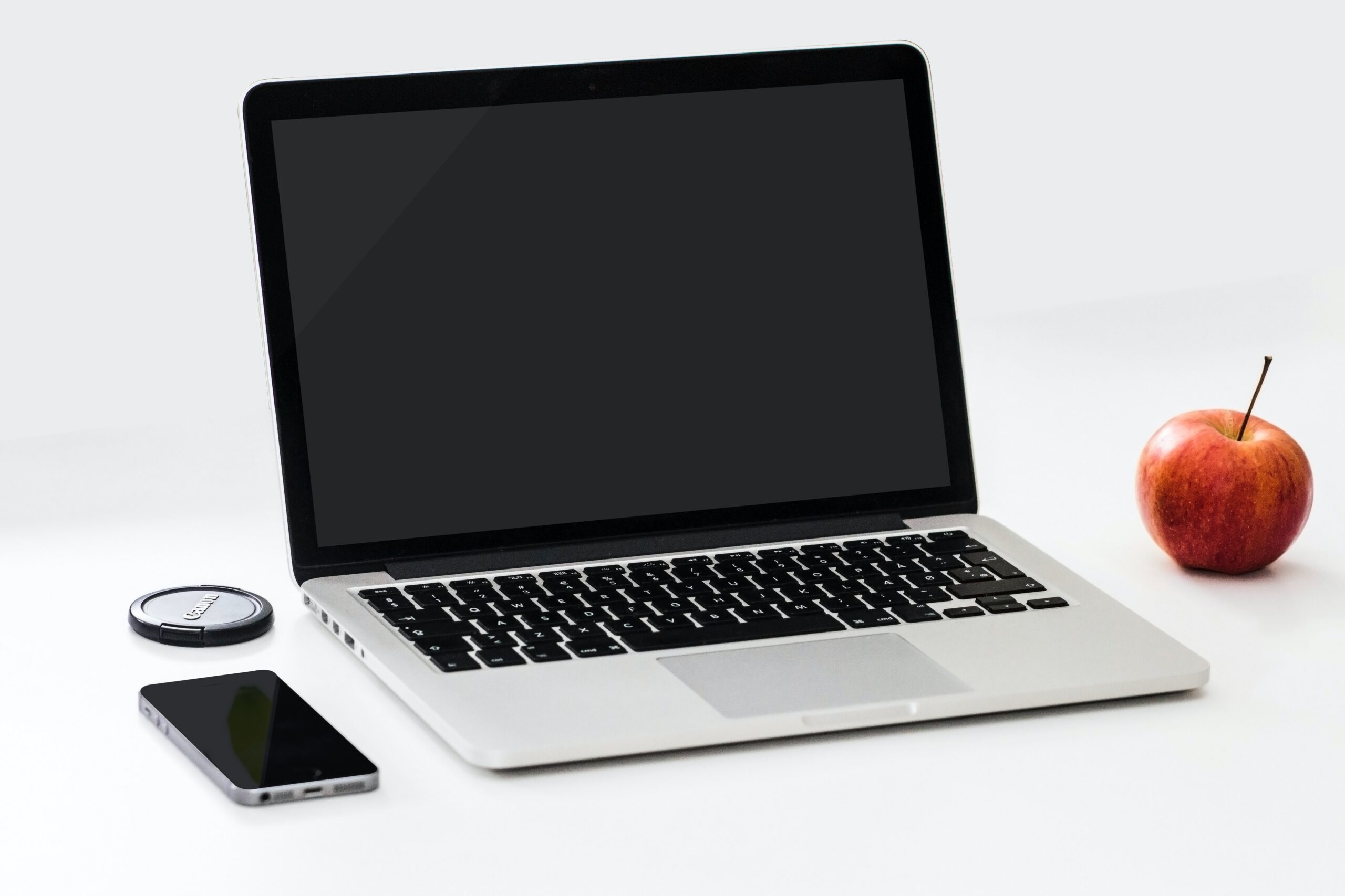 Laptop, telefon i jabłko leżące na białym stole na białym tle