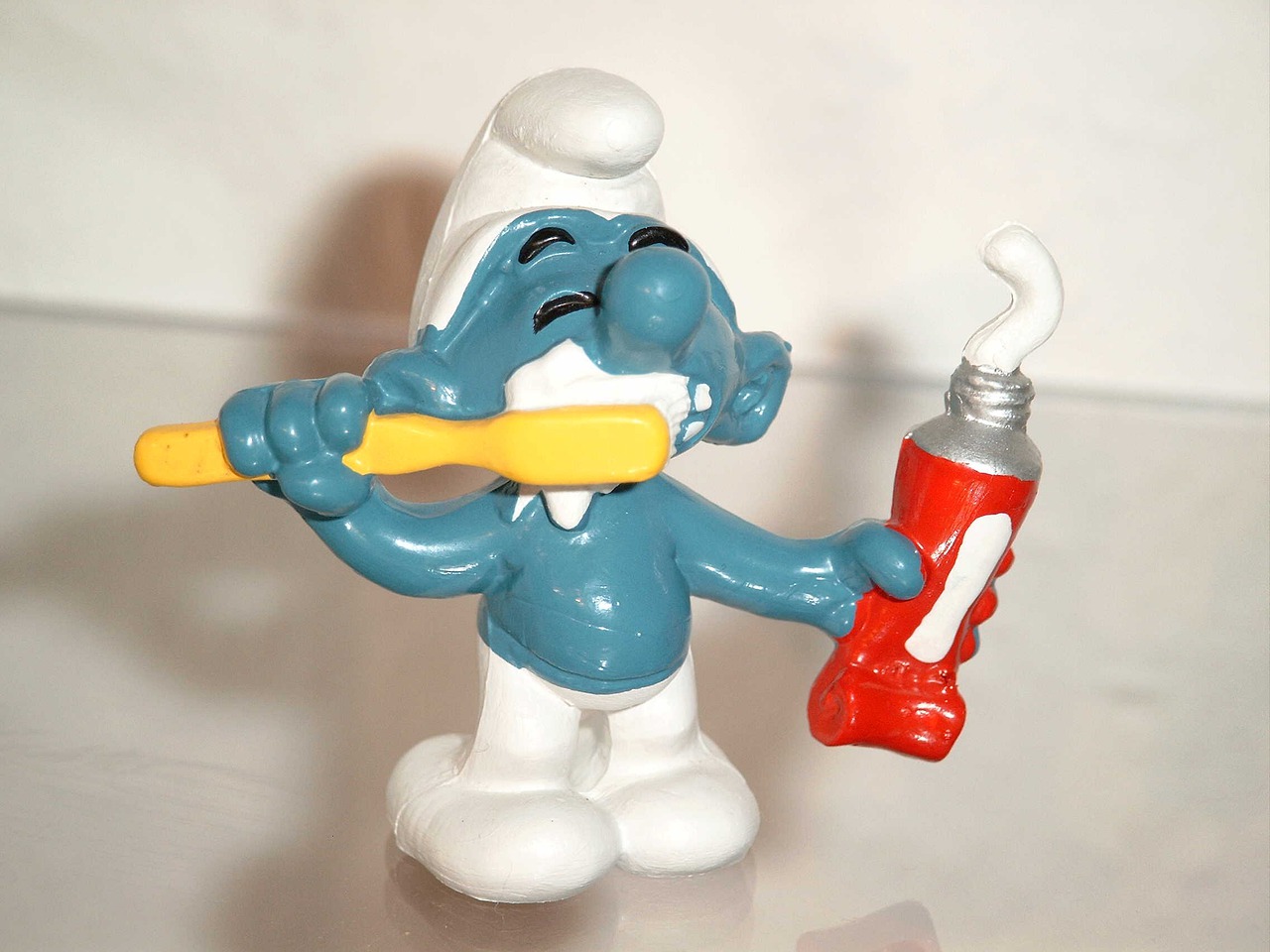 Figurka smerfa myjącego zęby szczoteczką i trzymający w ręce pastę do zębów