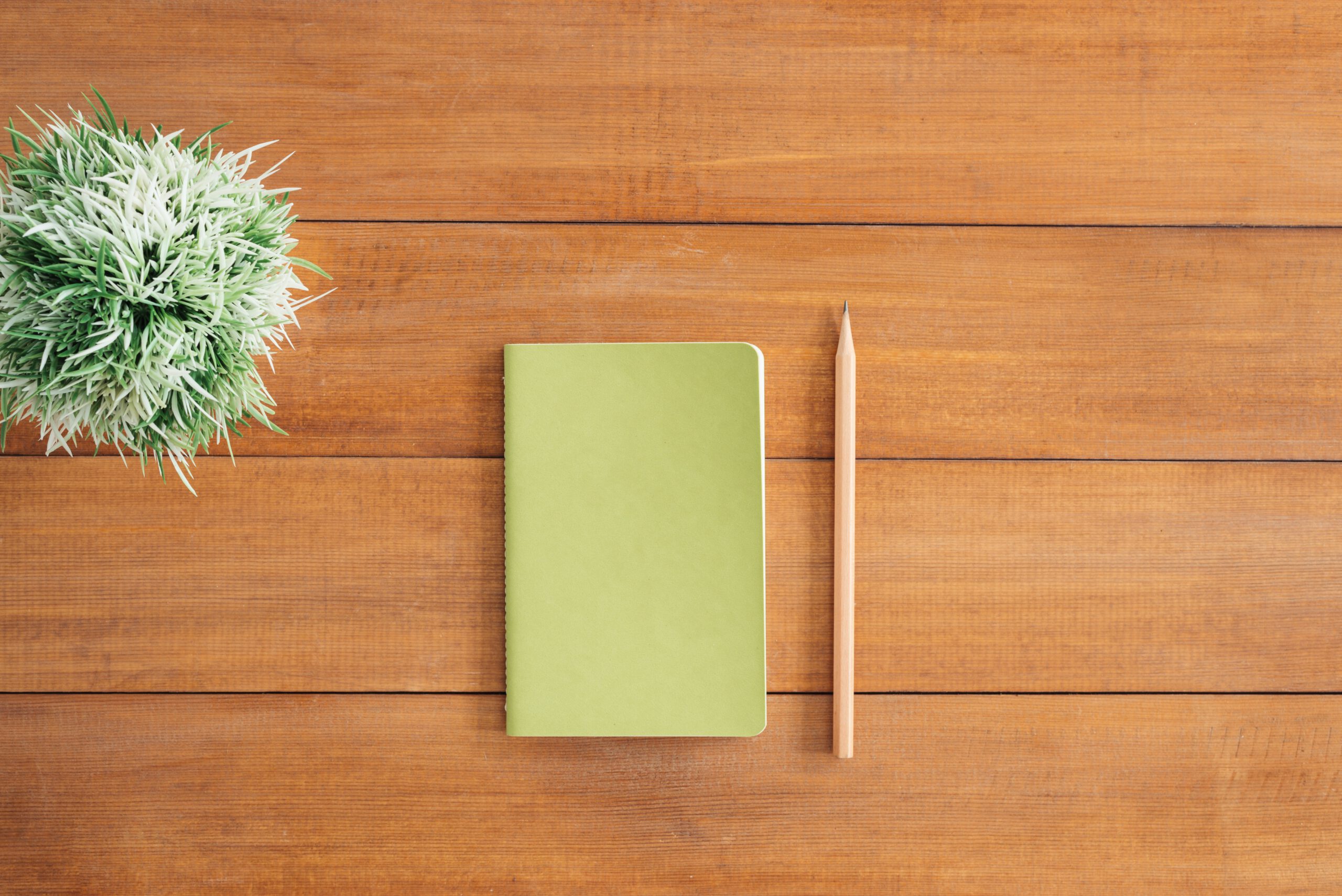 Zielony notatnik i ołówek leżące na drewnianym stole